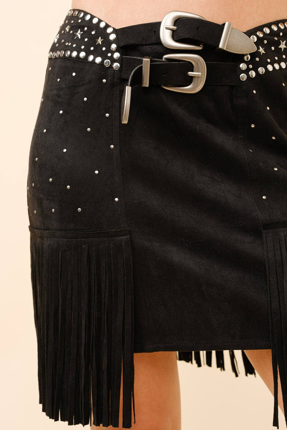 Black RARA Boutique suede mini skirt with double belts, star studs, and fringe detailing, styled for a trendy, edgy look.