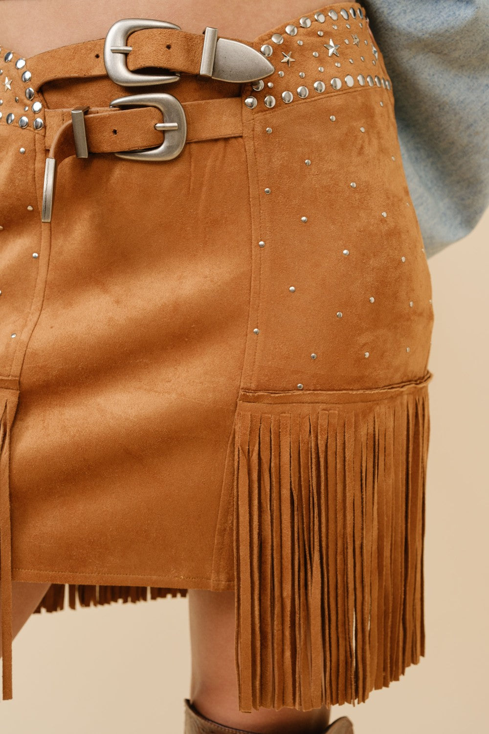 Blue suede mini skirt with double belts, star studs, and fringe detailing from RARA Boutique, featuring a stylish and edgy design.