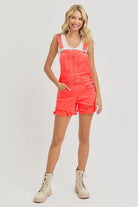 Risen distressed denim shorts overalls with a coral wash, featuring adjustable straps and rolled cuffs, casual summer style.