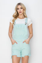 Risen distressed denim shorts overalls with a mint green wash, casual style, and adjustable straps, displayed on a hanger.