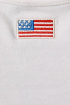White tank top featuring embroidered American flag patch and halter neck design by Le Lis, styled with casual and patriotic elements.